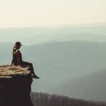 Risks - Woman Sitting on Edge of Rock Formation