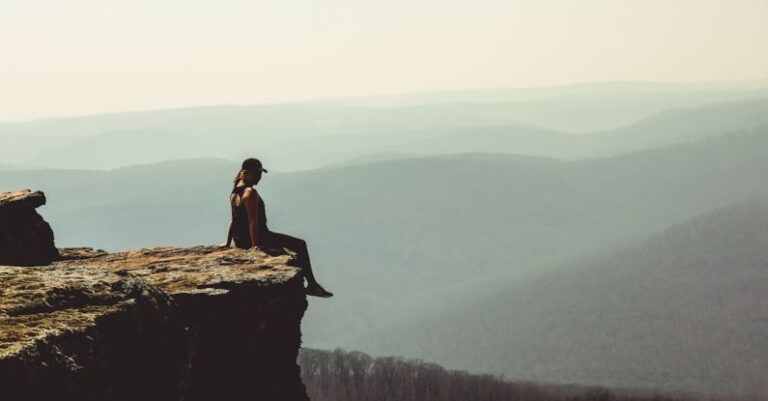 Risks - Woman Sitting on Edge of Rock Formation