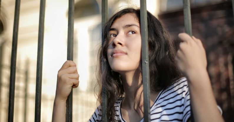 Opportunities - Sad isolated young woman looking away through fence with hope