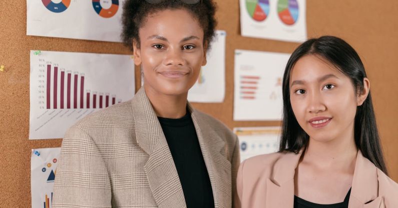 Analysts - Two Women in Corporate Attire in Front of Bulletin Board of Charts